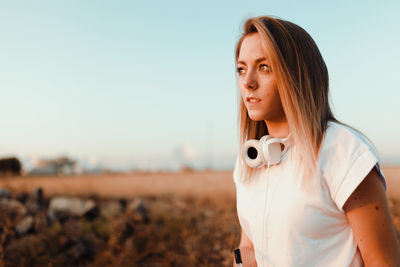 Young woman looking away while standing on field against sky