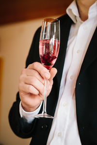 Midsection of man holding glass of sparkling red wine