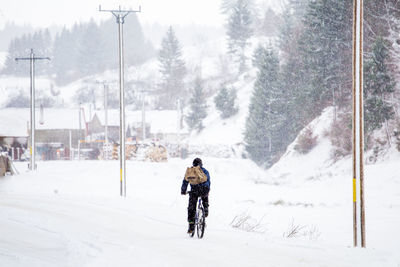 Rear view of man riding bicycle on snow covered landscape