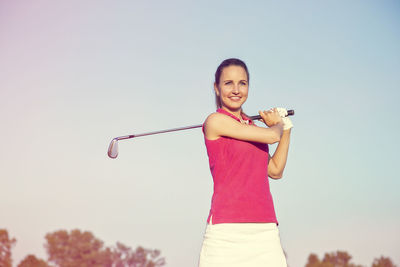 Portrait of smiling young man holding while standing against clear sky