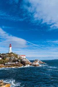 Lighthouse on sea by buildings against sky