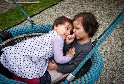High angle view of siblings lying on swing at playground