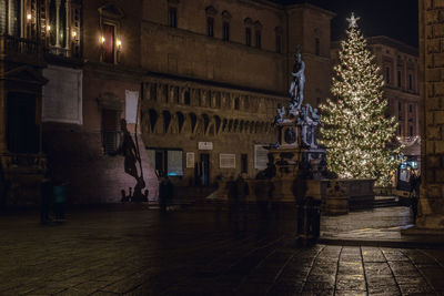 Illuminated christmas tree on street amidst buildings in city at night