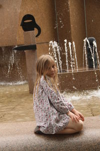 Girl kneeling on retaining wall by fountain