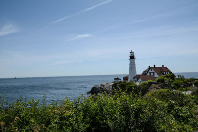 Lighthouse amidst sea and buildings against sky