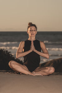 Full length of woman meditating at beach against sky