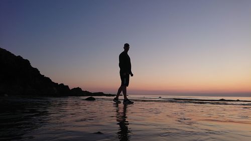 Silhouette man standing at beach against sky during sunset