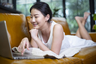 Young woman using laptop while lying down on sofa at home