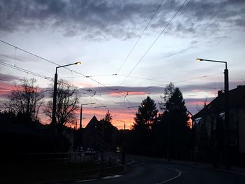 Silhouette trees by road against dramatic sky