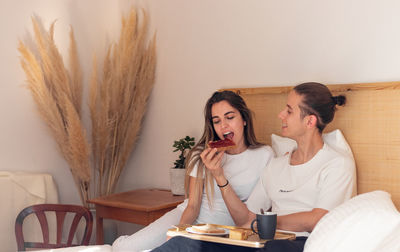 Happy young man and woman couple giving food to each other having breakfast in bed romantic date