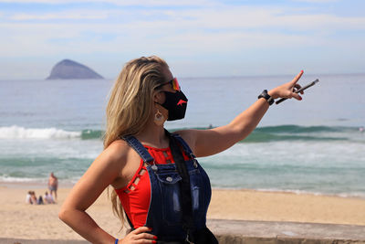 Young woman wearing sunglasses at beach against sky