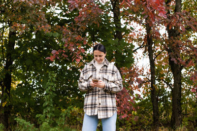 A girl in warm clothes on the background of a forest with a phone in her hands
