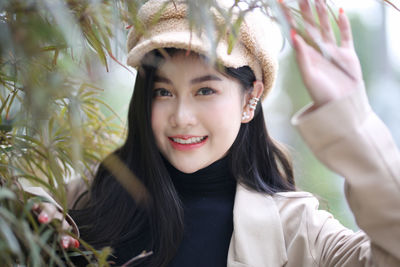 Portrait of beautiful young woman standing by tree during winter