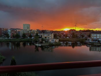 Buildings by river against sky during sunset