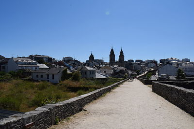 Footpath amidst buildings in city against clear blue sky