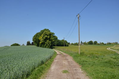 Road amidst field against clear blue sky