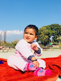 Cute baby girl sitting on blanket at beach during summer