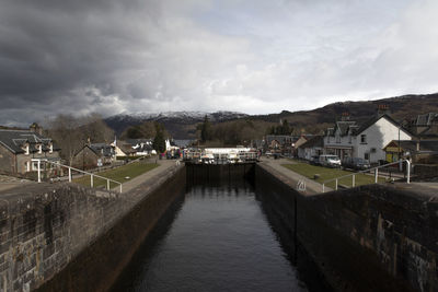 Houses by river amidst buildings against sky