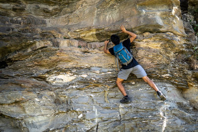 Young boy climbing the rocks wearing a backpack.