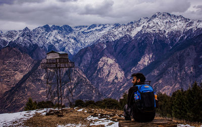 Rear view of backpacker sitting on log against snow covered mountain