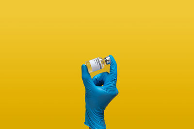 Close-up of hand holding smart phone against yellow background