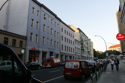 Cars on city street by buildings against clear sky