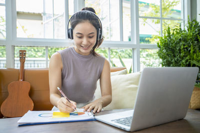 Young woman writing on document while sitting at greenhouse