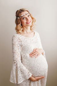 Portrait of smiling pregnant woman touching abdomen against white background