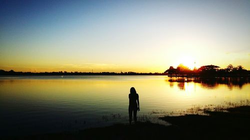 Rear view of silhouette man standing by lake against sky during sunset