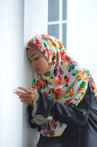 Teenage girl wearing headscarf using mobile phone while standing indoors