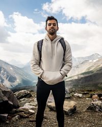 Portrait of young man standing on rock against sky