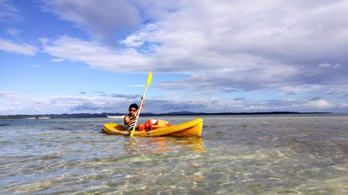 Man sailing boat in sea against cloudy sky