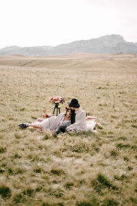 People sitting on field by mountain against sky