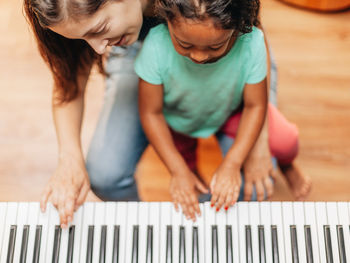 Happy mother teaching piano to daughter at home