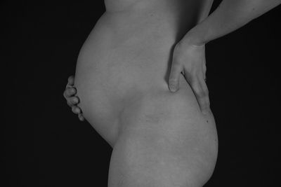 Midsection of naked pregnant woman against black background