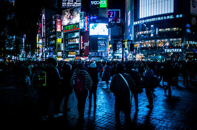 Crowd walking on illuminated city street at night