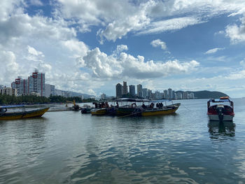Boats moored in river by buildings against sky