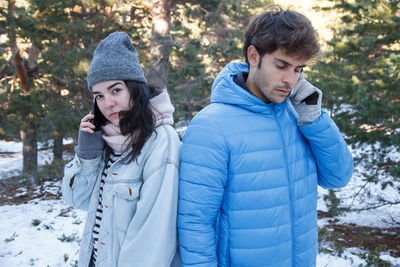 Couple talking on mobile phone while standing on snow covered field