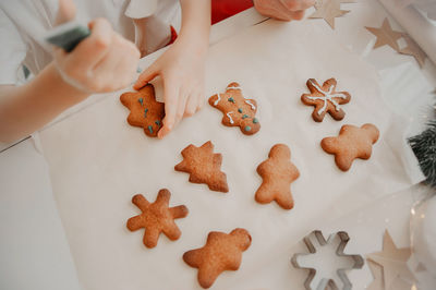 Hands paint with a dye from a tube on cookies, finished cookies on a white table with baking paper