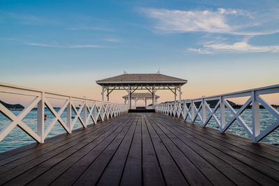 Wooden footbridge leading to pier on sea against sky