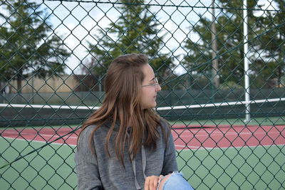 Young woman looking through chainlink fence