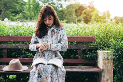 Young woman checking time while sitting on bench at park