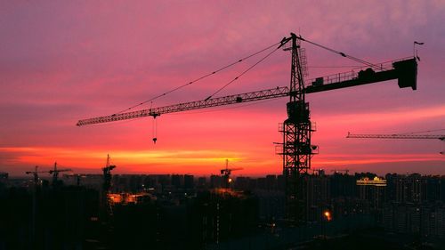 Silhouette of cranes at construction site during sunset