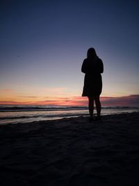 Rear view of silhouette woman standing on beach during sunset