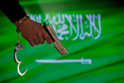 Cropped hand with handcuffs holding gun against saudi arabian flag