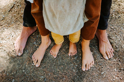 From above of barefoot legs of crop family standing together on ground in forest on sunny day