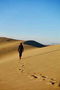 Rear view of woman walking on sand at desert against blue sky