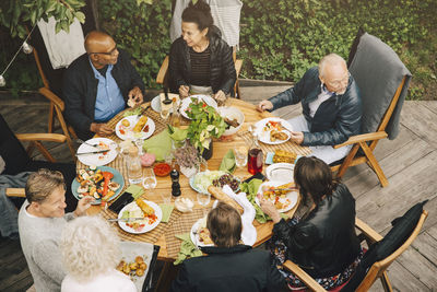 High angle view of senior friends enjoying meal at dining table during garden party at back yard