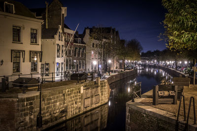 Canal by illuminated buildings against sky at night