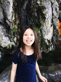 Portrait of smiling young woman standing on rock against trees